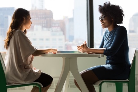 An image of two people sitting at a table, smiling, and talking to each other.